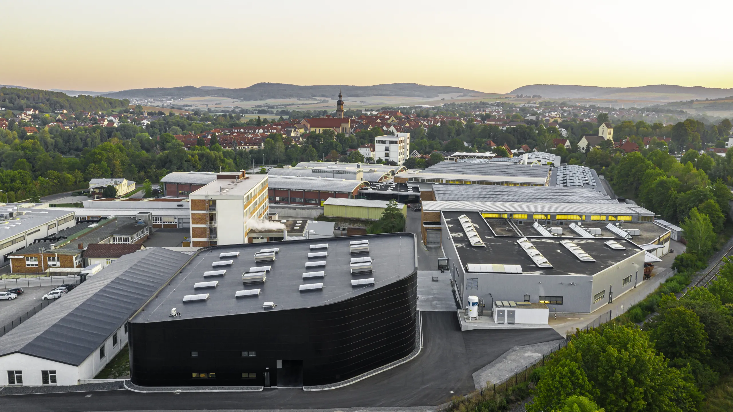 Eine Luftaufnahme bei Sonnenuntergang mit dem Produktionsgelaende der Reich GmbH im Vordergrund und Mellrichstadt und Bergen im Hintergrund 