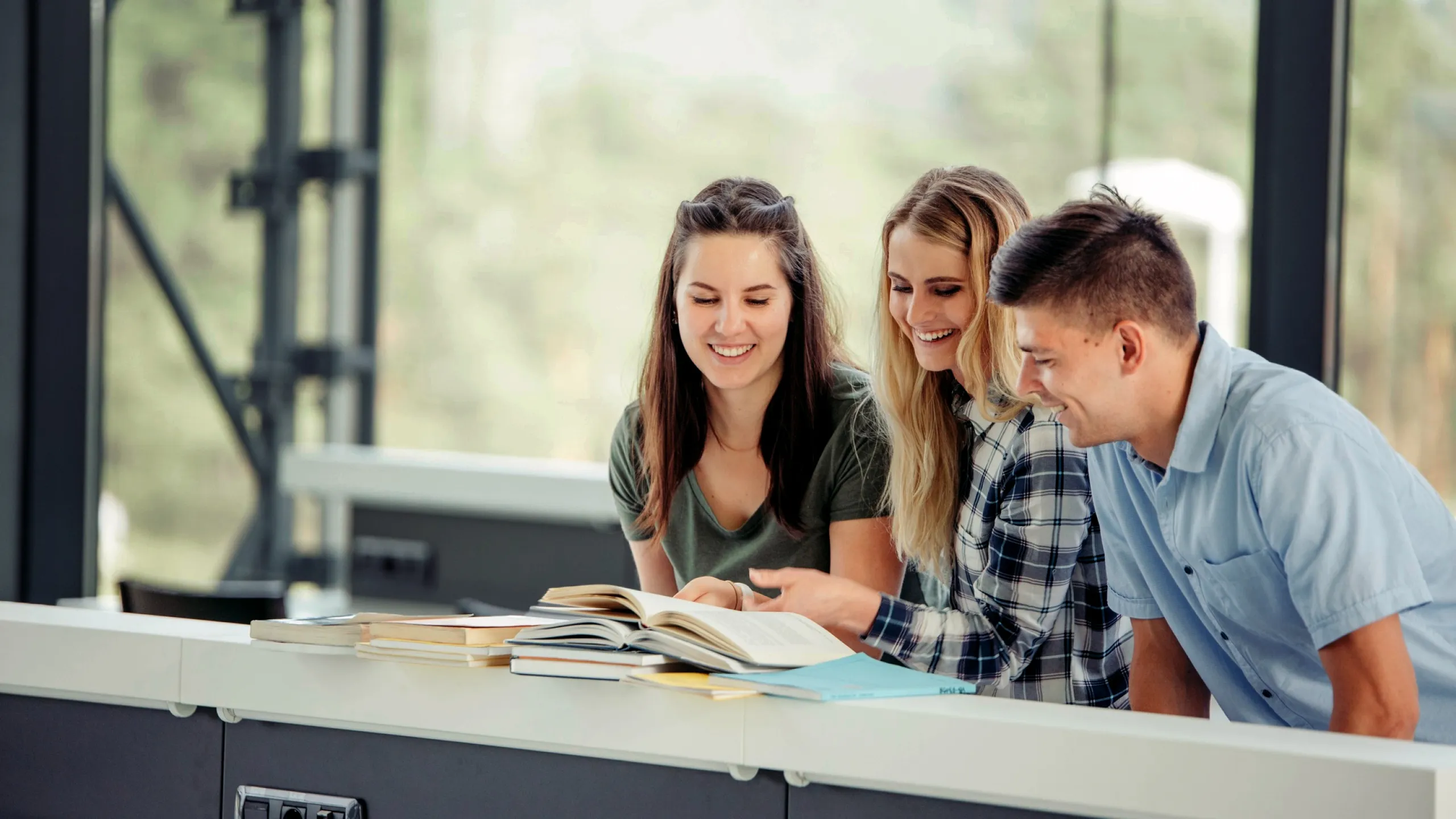 Drei Studenten schauen lachend gemeinsam in ein Buch. 