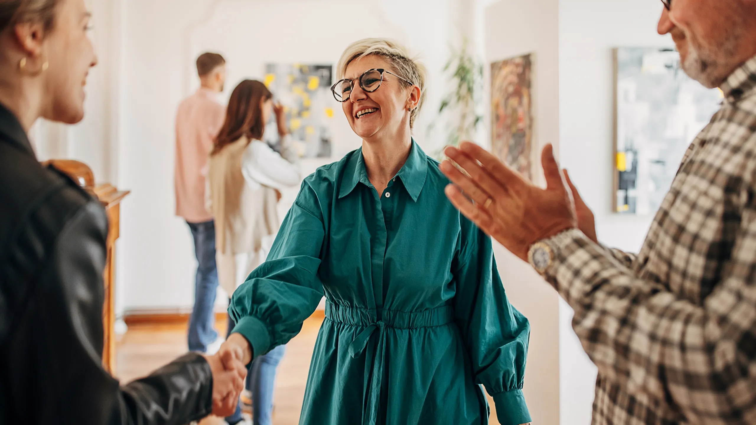 Frau schüttelt lächelnder Frau in einer Galerie die Hand. 