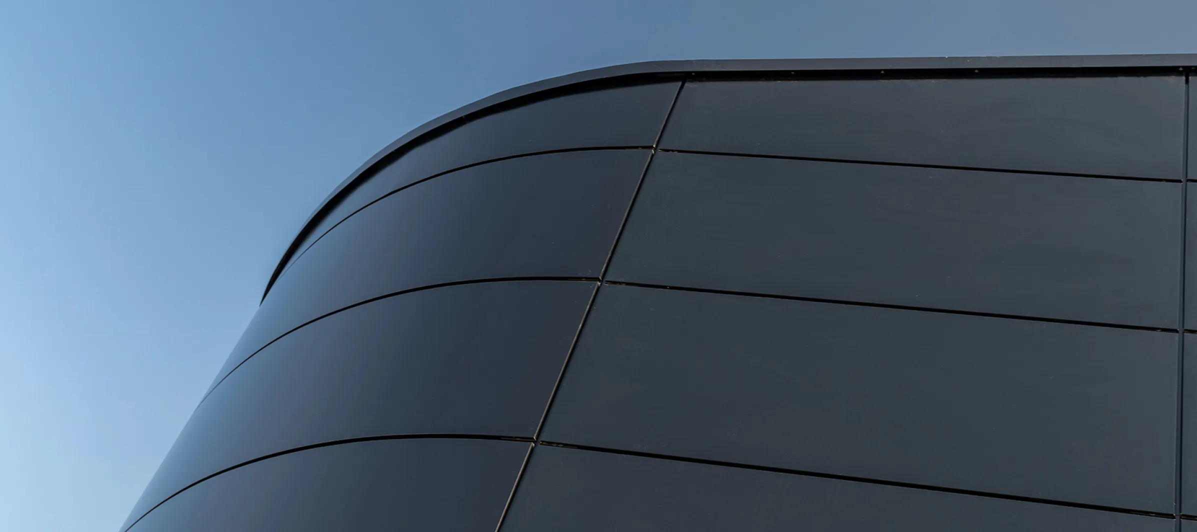 Ecke einer schwarzen Produktionshalle von Reich aus der Froschperspektive mit dem Himmel im Hintergrund.