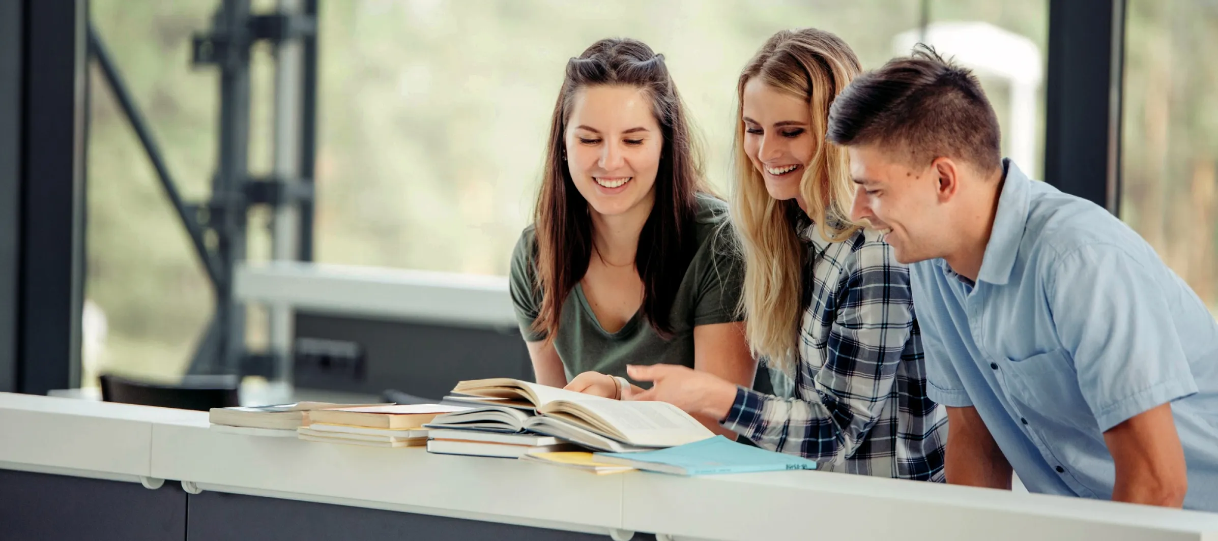 Drei Studenten schauen lachend gemeinsam in ein Buch.