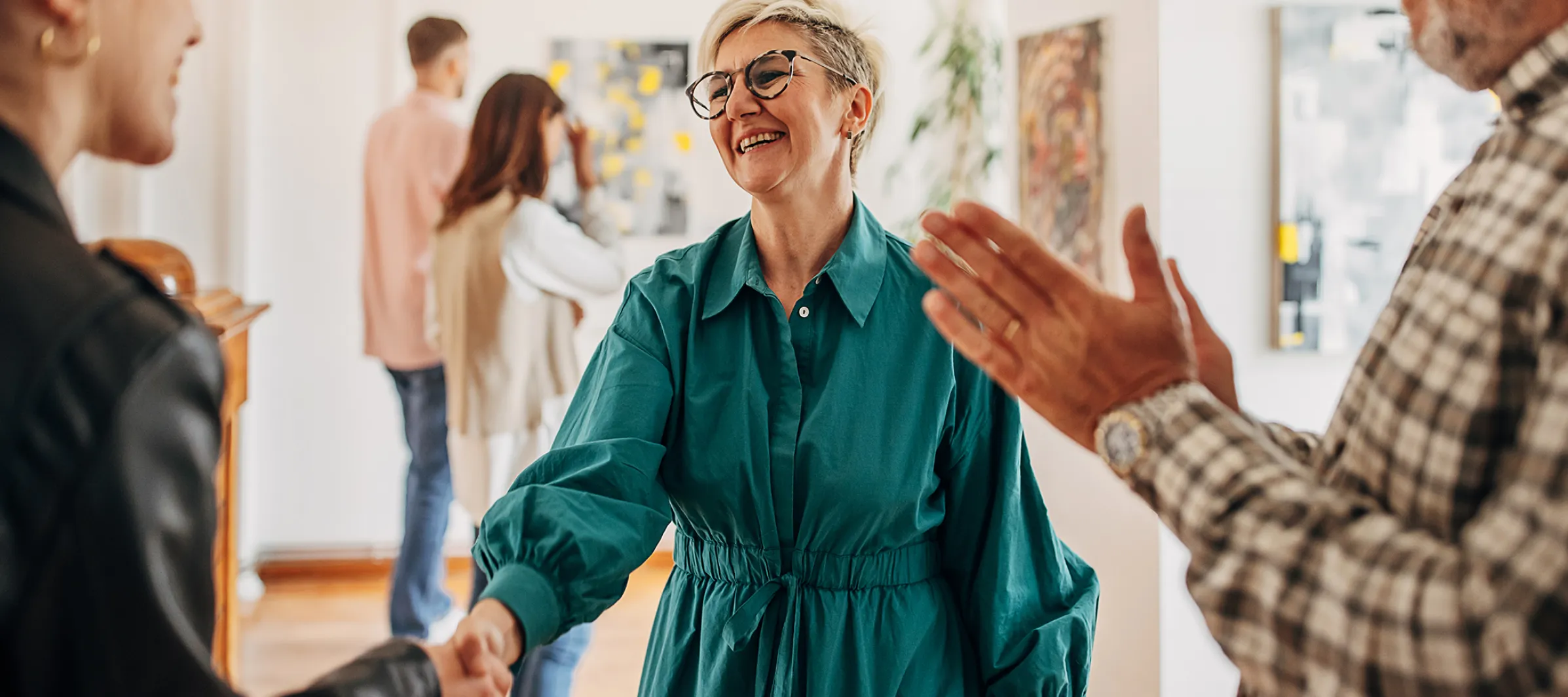 Frau schüttelt lächelnder Frau in einer Galerie die Hand. 